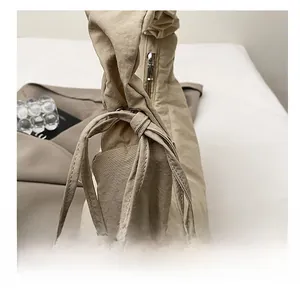 Close-up of beige dumpling bag featuring ruched handle, metal zipper and pleated fabric detail