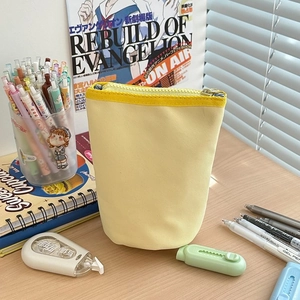 Vertical yellow canvas pencil pouch with zipper detail on a cozy stationery desktop