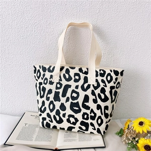 Detail view of leopard print canvas tote bag with cream-colored handles and lifestyle props