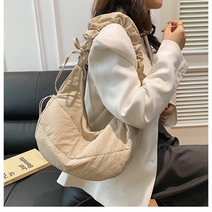 Detail of a beige ruched hobo bag with drawstring strap on a black leather sofa