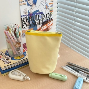 Standing pale yellow canvas pen case with zipper detail on a wooden desk background