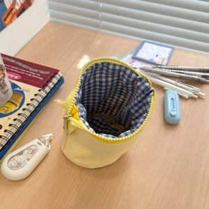 Detail shot of a yellow cylindrical pencil pouch with blue and white plaid inner lining