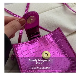 Close-up of fuchsia crocodile pattern leather bag featuring a gold magnetic snap closure