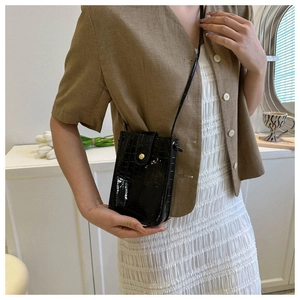 Detail of black faux crocodile leather phone bag with gold clasp shown on a shoulder
