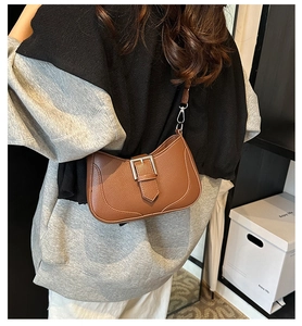 Brown lychee-grain crescent bag with silver buckle worn over the shoulder by a model