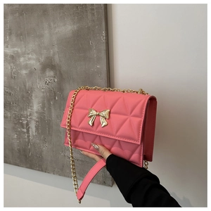 Close-up of pink quilted crossbody bag featuring a golden metal bow and elegant chain strap