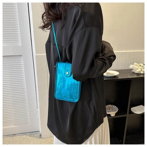 Detail of blue faux-crocodile patent leather crossbody phone bag shown on shoulder