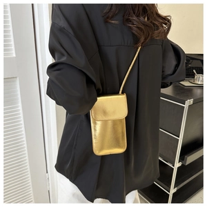 Détail d'un sac à téléphone doré métallisé avec rabat et bandoulière ronde sur un mannequin