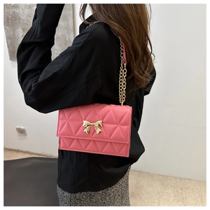 Detail of pink quilted crossbody bag featuring a golden bow metal clasp and chain strap