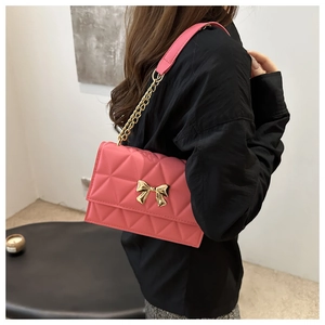 Pink quilted crossbody bag with gold bow clasp and metal chain strap on model shoulder