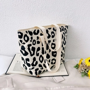 Detailed view of pink leopard print canvas tote bag with wide shoulder straps in a cozy setting