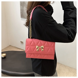 Detailed shot of pink quilted crossbody bag featuring a gold bow buckle and chain strap
