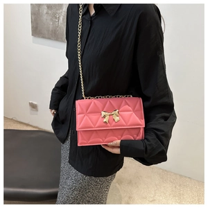 Detail of pink quilted crossbody bag featuring golden bow clasp and chain strap on model