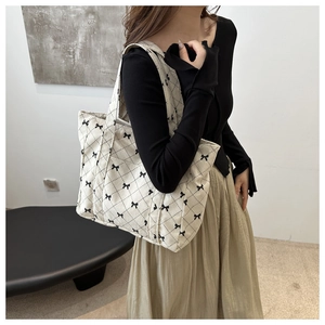 Detail of a beige tote bag with black bow pattern and quilted texture on a model