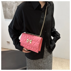 Detail view of pink quilted handbag with gold chain strap and metal bow lock on pink bag