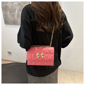 Detail showing the pink quilted crossbody bag with a golden bow and chain strap on model