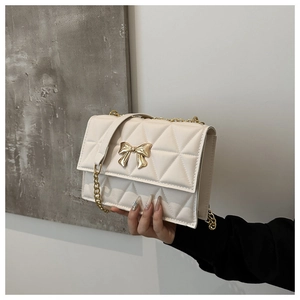 Detail of cream quilted crossbody bag with gold bow clasp and metallic chain strap