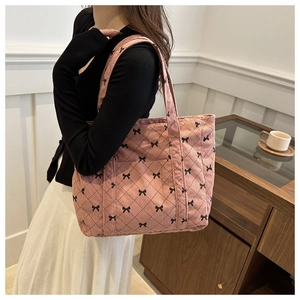 Pink corduroy tote bag with black bow patterns shown on shoulder in cozy indoor setting