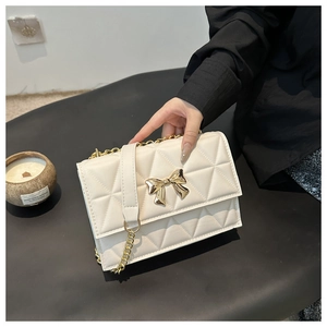 Close-up of quilted cream crossbody bag with gold bow clasp and metallic chain strap
