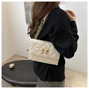 Detail of quilted leather crossbody bag with golden bow clasp and chain strap