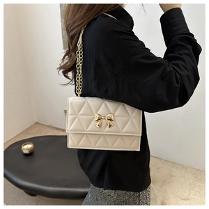 Detail view of white quilted crossbody bag with gold bow clasp and metal chain strap