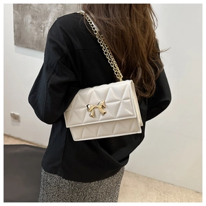 Detail of cream quilted crossbody bag featuring a gold bow clasp and metallic chain