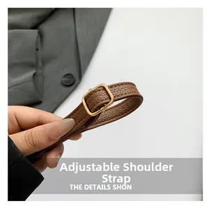 Detail of adjustable shoulder strap with gold metal buckle on brown leather bag