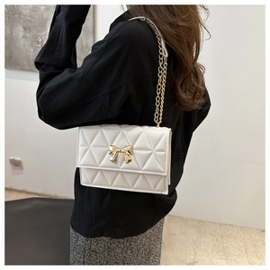 Close-up of white quilted crossbody bag with golden bow clasp and chain strap detail