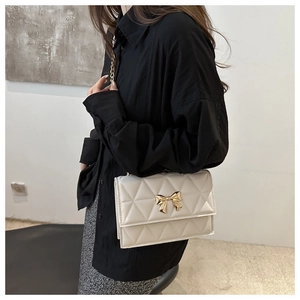 Detail showing the creamy white quilted texture and golden bow hardware of the crossbody bag