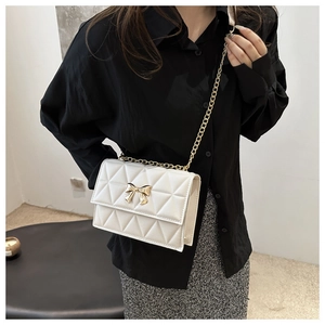 Detail view of a white quilted shoulder bag with golden bow and chain strap on model