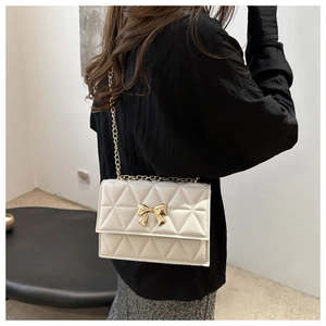 Detail of cream quilted crossbody bag with gold bow clasp and metallic chain strap