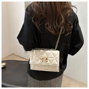 Close-up of quilted cream crossbody bag with golden bow detail on model shoulder