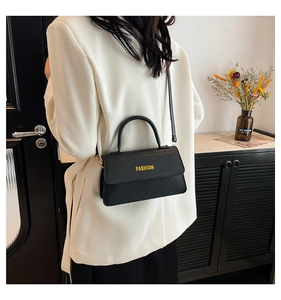 Detail of black pebbled leather crossbody bag with Fashion lettering shown on a model