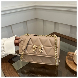 Detailed close-up of quilted beige crossbody bag with golden bow clasp and metal chain strap