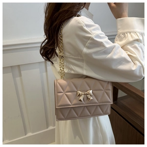 Detail shot of apricot quilted crossbody bag with golden bow clasp on model