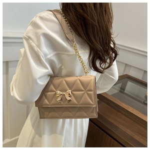 Detail view of beige quilted crossbody bag with golden bow hardware and chain strap