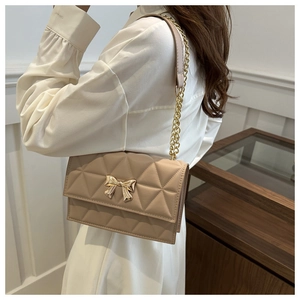Detail of beige quilted shoulder bag featuring golden bow clasp and chain strap