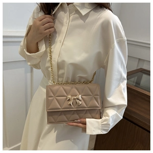 Detail of quilted beige shoulder bag featuring a golden bow buckle and chain strap