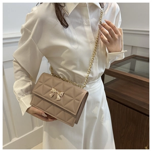 Detail of beige quilted crossbody bag featuring a golden bow buckle and chain strap