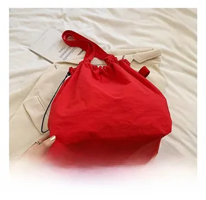 Close-up of vibrant red nylon bucket bag with drawstring on a stylish beige jacket