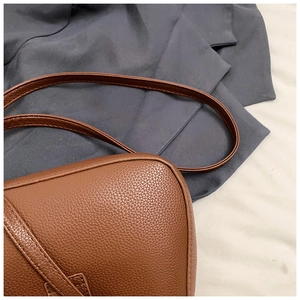 Close-up detail of the brown pebble leather texture and uniform stitching on the crescent bag
