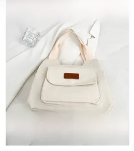 Dettaglio della borsa tote in tela beige con tasca anteriore e etichetta in pelle