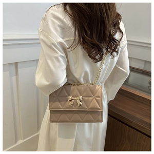 Detail of beige quilted shoulder bag with golden bow clasp and metal chain strap