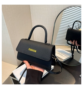 Detail of black pebbled leather handbag with yellow FASHION print and gold metal hardware