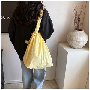 Detail showing the drawstring closure of this light yellow nylon bucket shoulder bag