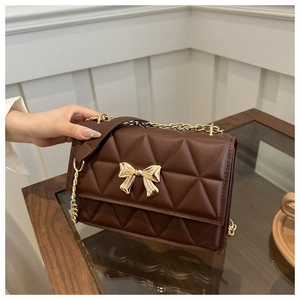 Detail of deep brown quilted shoulder bag featuring golden bow metal lock and chain strap
