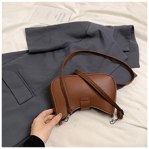 Detailed view of brown litchi leather crescent bag with silver buckles on white background