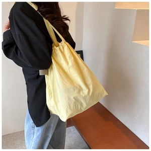 Side view of a vibrant yellow nylon bucket bag worn by a model in a minimalist setting