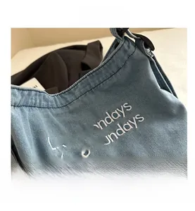 Detail of light blue denim tote bag with Less Mondays More Sundays embroidery and strap