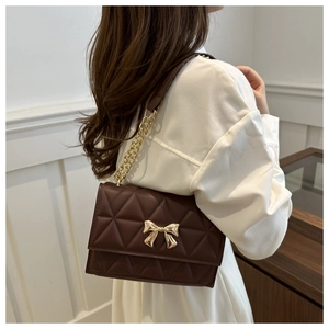 Detail of a dark brown quilted shoulder bag featuring a gold bow buckle on a model